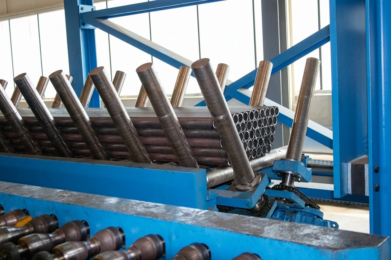 IGEMA Technology GmbH&Co.KG -  Maschinenbau & Verpackungstechnik Service - Gestapelte Bündel industrieller Metallrohre warten auf einer Fertigungslinie.