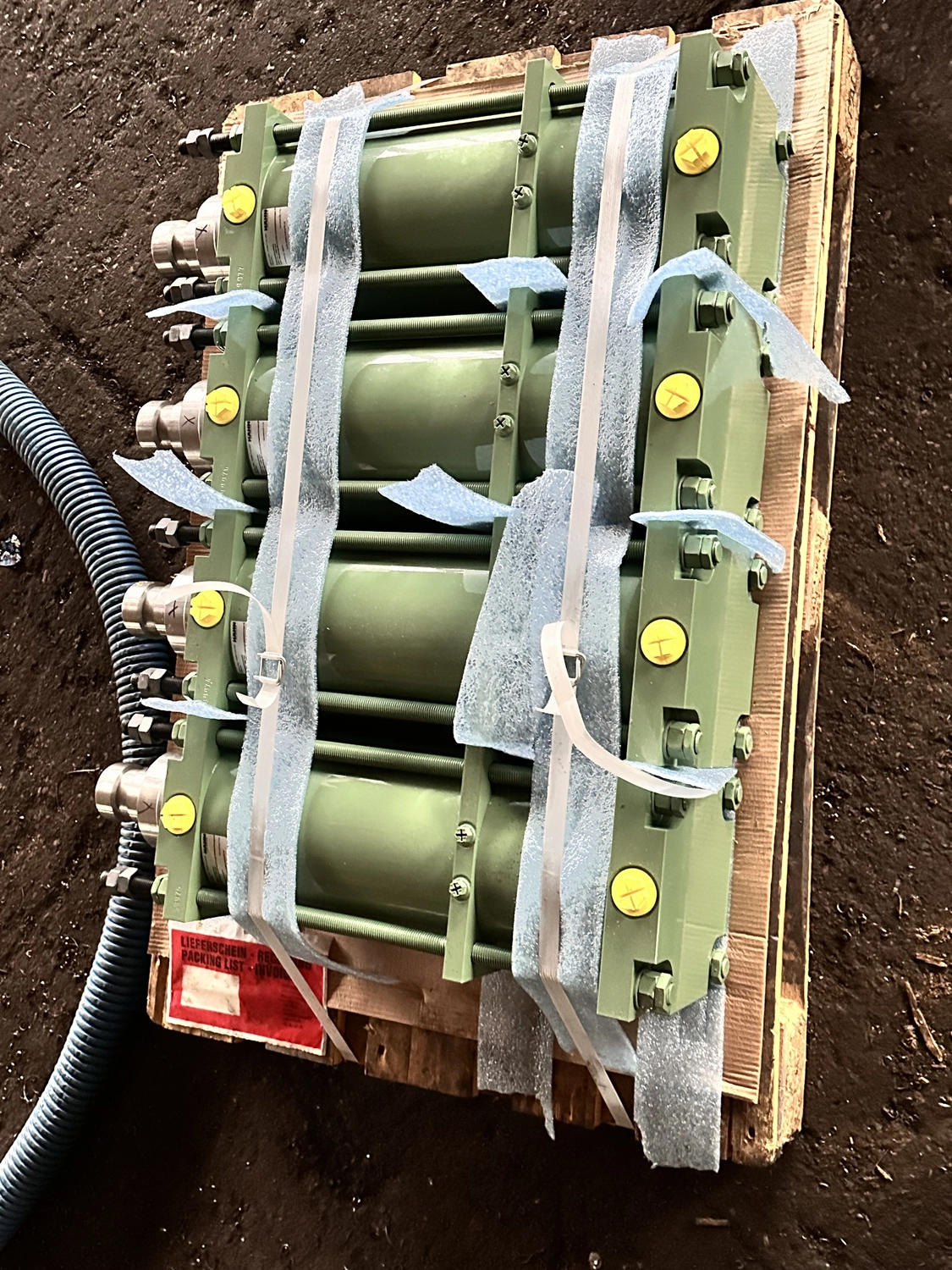 IGEMA Technology GmbH&Co.KG - Maschinenbau & Verpackungstechnik Service - Mehrere grüne Industriehydraulikzylinder, fest auf einer Holzpalette zusammengebunden.