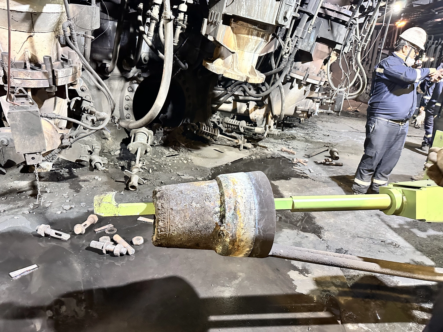 IGEMA Technology GmbH&Co.KG - Maschinenbau & Verpackungstechnik Service - Ein Arbeiter in Schutzausrüstung bedient einen großen mechanischen Kolben in der Nähe schwerer Fabrikmaschinen.