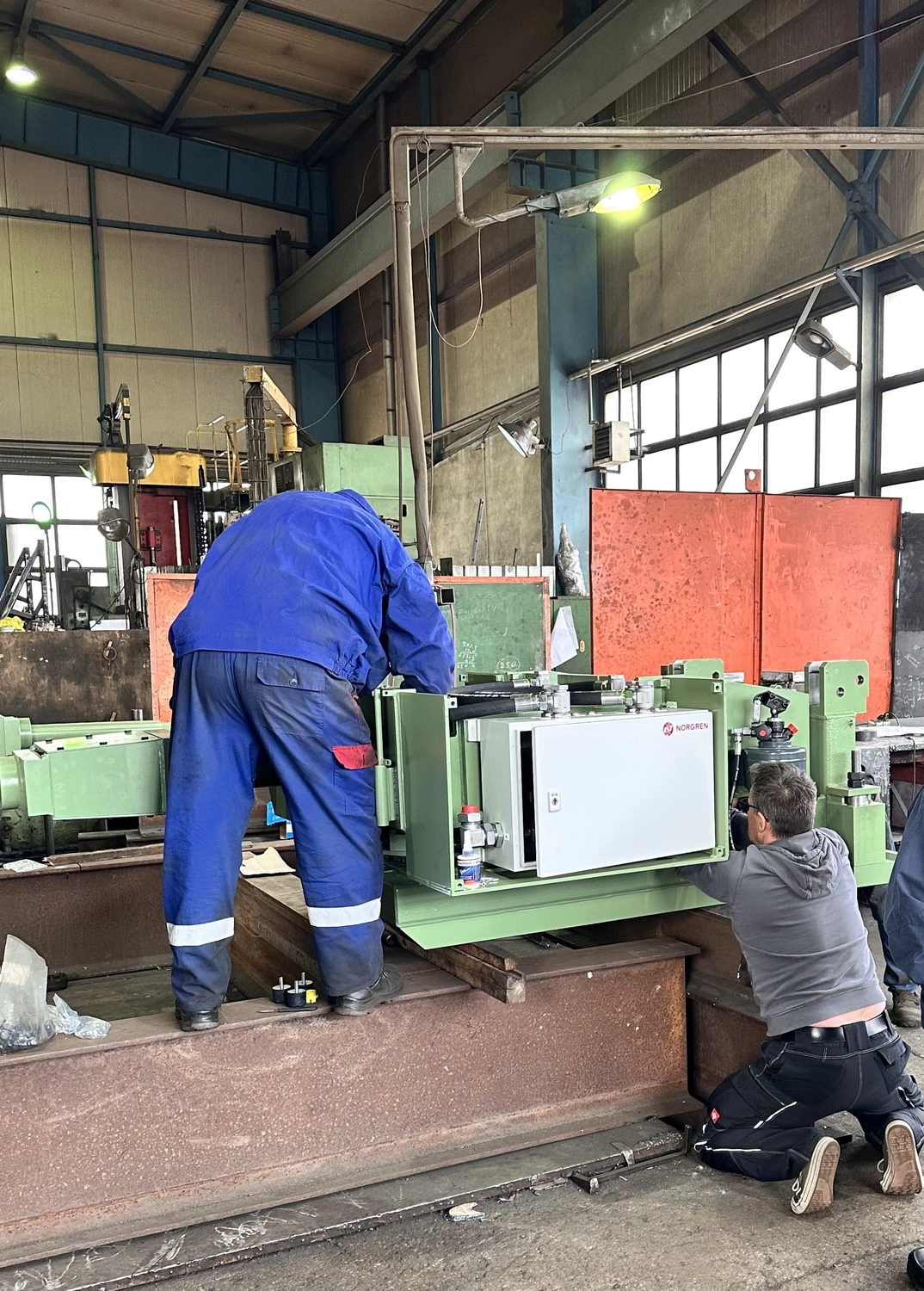 IGEMA Technology GmbH&Co.KG - Maschinenbau & Verpackungstechnik Service - Zwei Techniker montieren in einer Werkstatt elektrische Bauteile an einer schweren, grünen Industriemaschine.