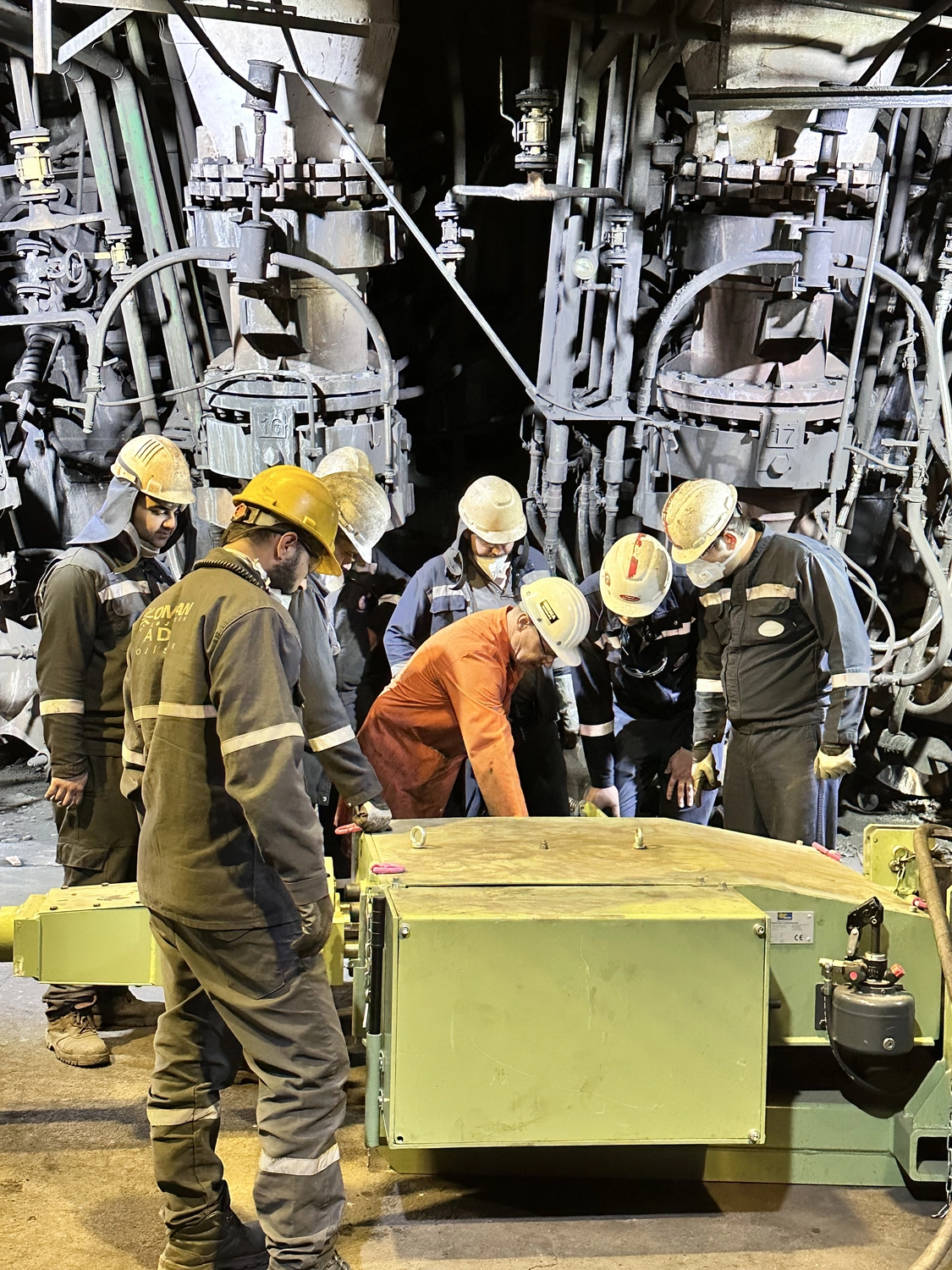 IGEMA Technology GmbH&Co.KG - Maschinenbau & Verpackungstechnik Service - Industriearbeiter mit Schutzhelmen und Uniformen versammeln sich zur Wartung einer großen Maschine in einer Produktionsanlage. Send feedback