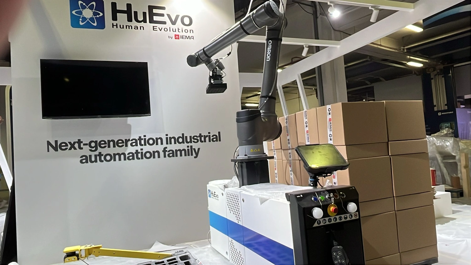 IGEMA Technology GmbH&Co.KG - Maschinenbau & Verpackungstechnik Service - Ein mobiles kollaboratives Robotersystem (Cobot) zum Palettieren steht neben gestapelten Kartons vor einem HuEvo-Logo.