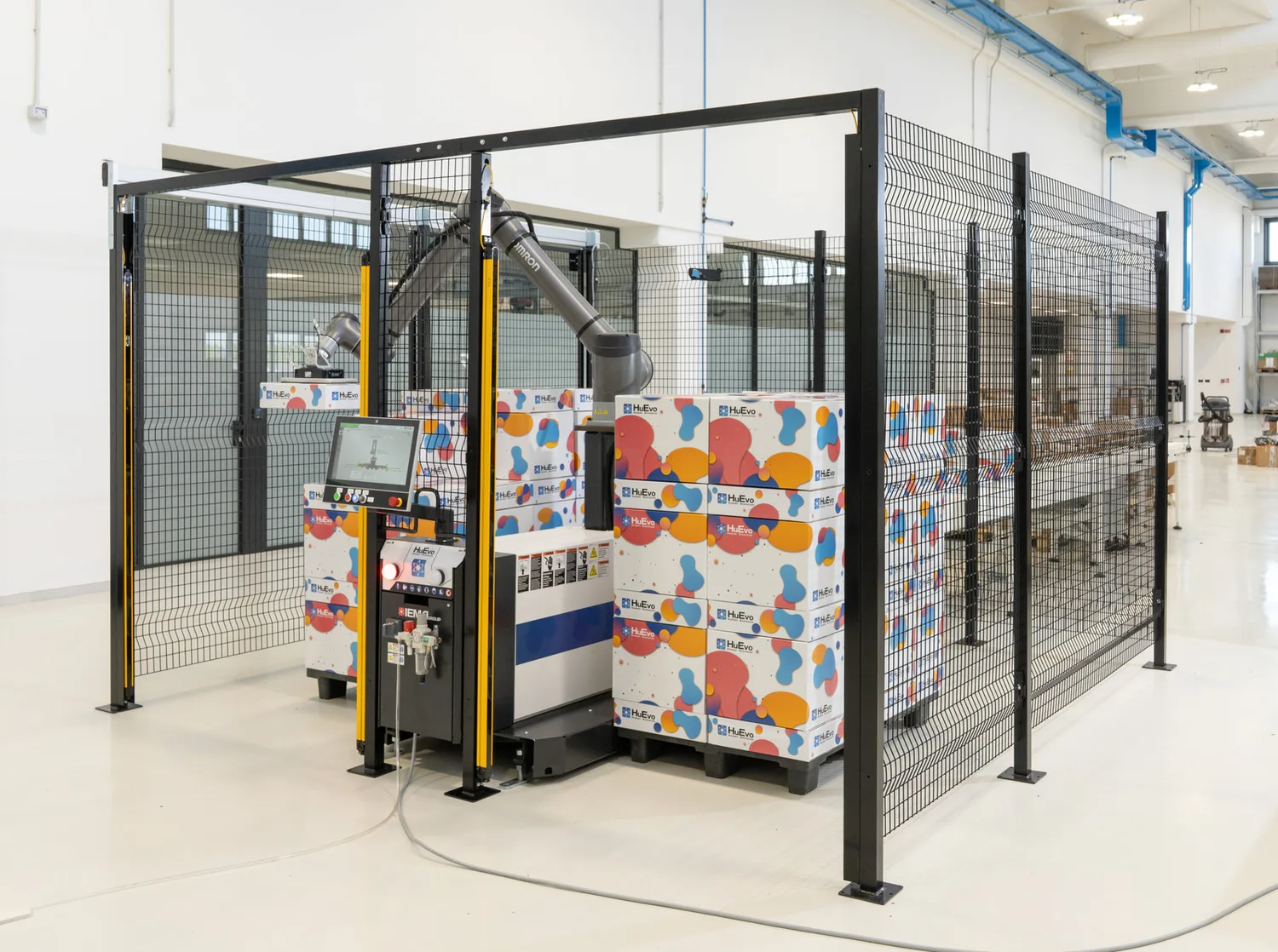 IGEMA Technology GmbH&Co.KG - Maschinenbau & Verpackungstechnik Service - Ein Roboterarm palettiert bunte Kartons auf Paletten in einer schützenden, schwarzen Drahtgitterbox.