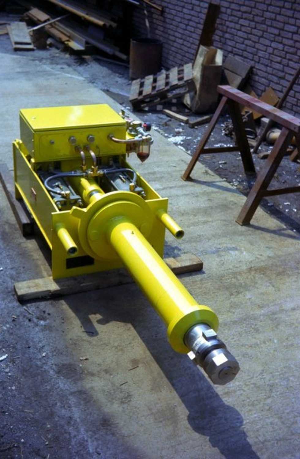 IGEMA Technology GmbH&Co.KG -  Maschinenbau & Verpackungstechnik Service - Ein gelber Hydraulikzylinder mit Pumpeneinheit auf Holzblöcken.