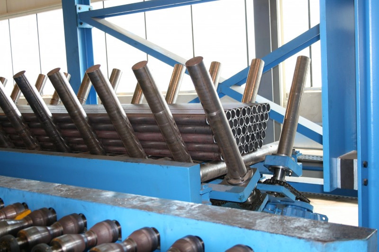 IGEMA Technology GmbH&Co.KG -  Maschinenbau & Verpackungstechnik Service - Gestapelte Bündel industrieller Metallrohre warten auf einer Fertigungslinie.